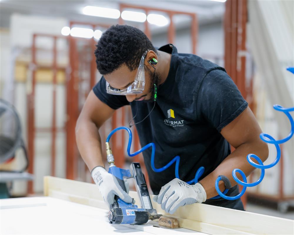 Employé d'Intermat assemblant un cadre de porte prémonté dans l'atelier de fabrication pour un projet de construction résidentiel ou commercial.